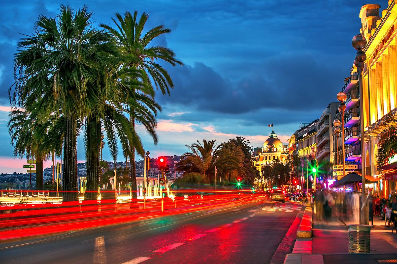 Dusk on a street lit up with buildings on one side and palm trees on the other
