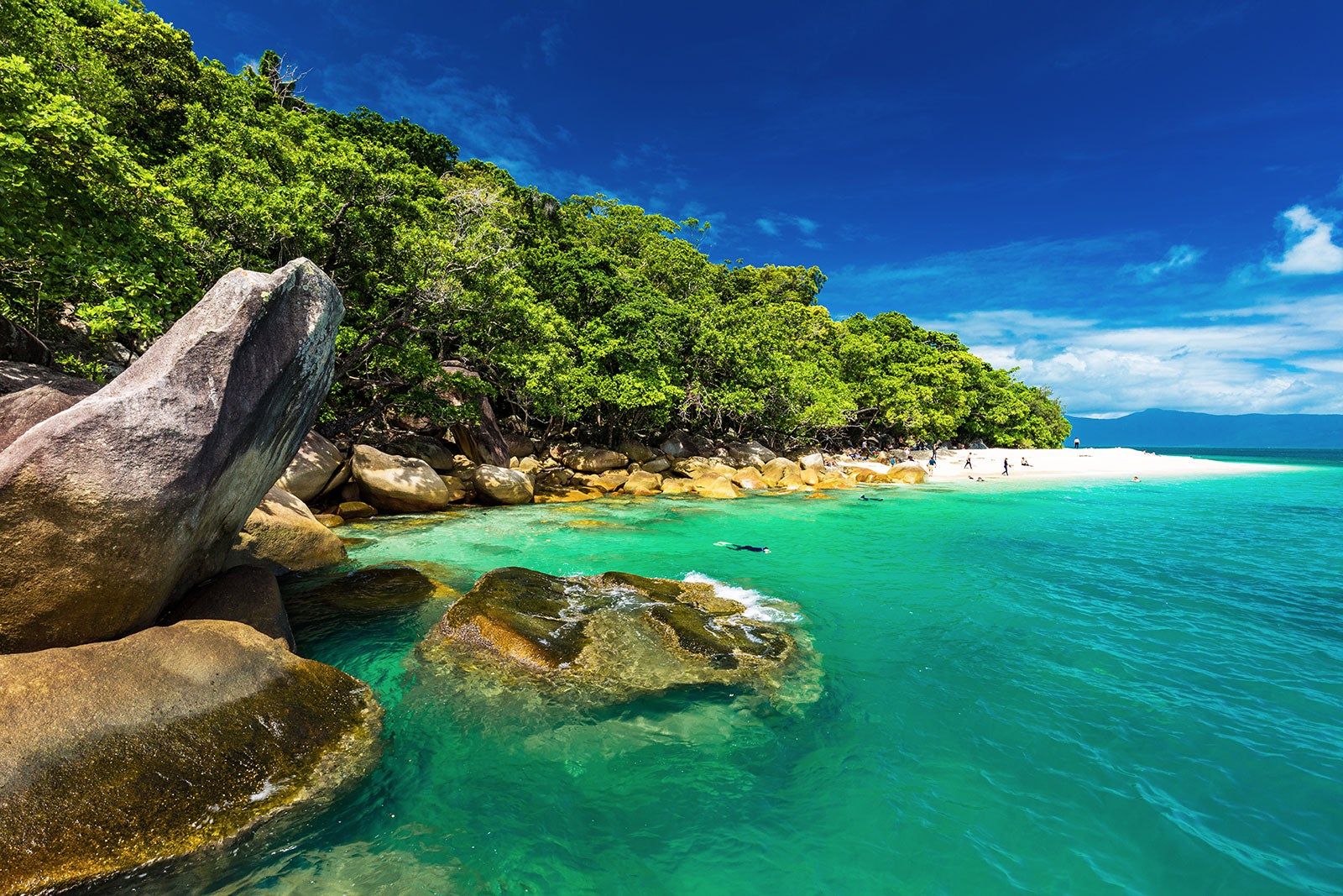 A beach surrounded by a hill with green trees.