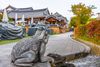 A statue of a frog next to a flowing stream of water with temple in the background.