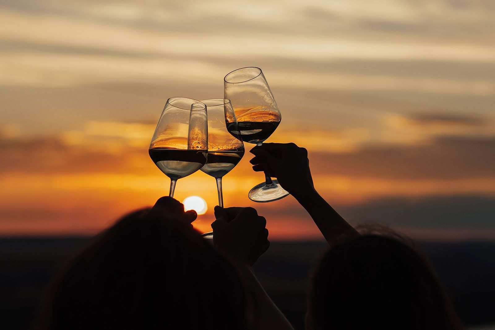 Three wine glasses clinked together at sunset.