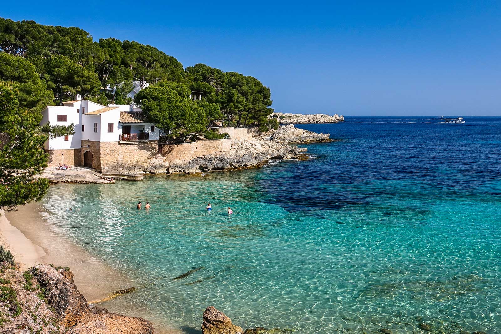 Small sandy beach, a white house on a cliff, people swimming crystal-clear water.