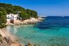 Small sandy beach, a white house on a cliff, people swimming crystal-clear water.