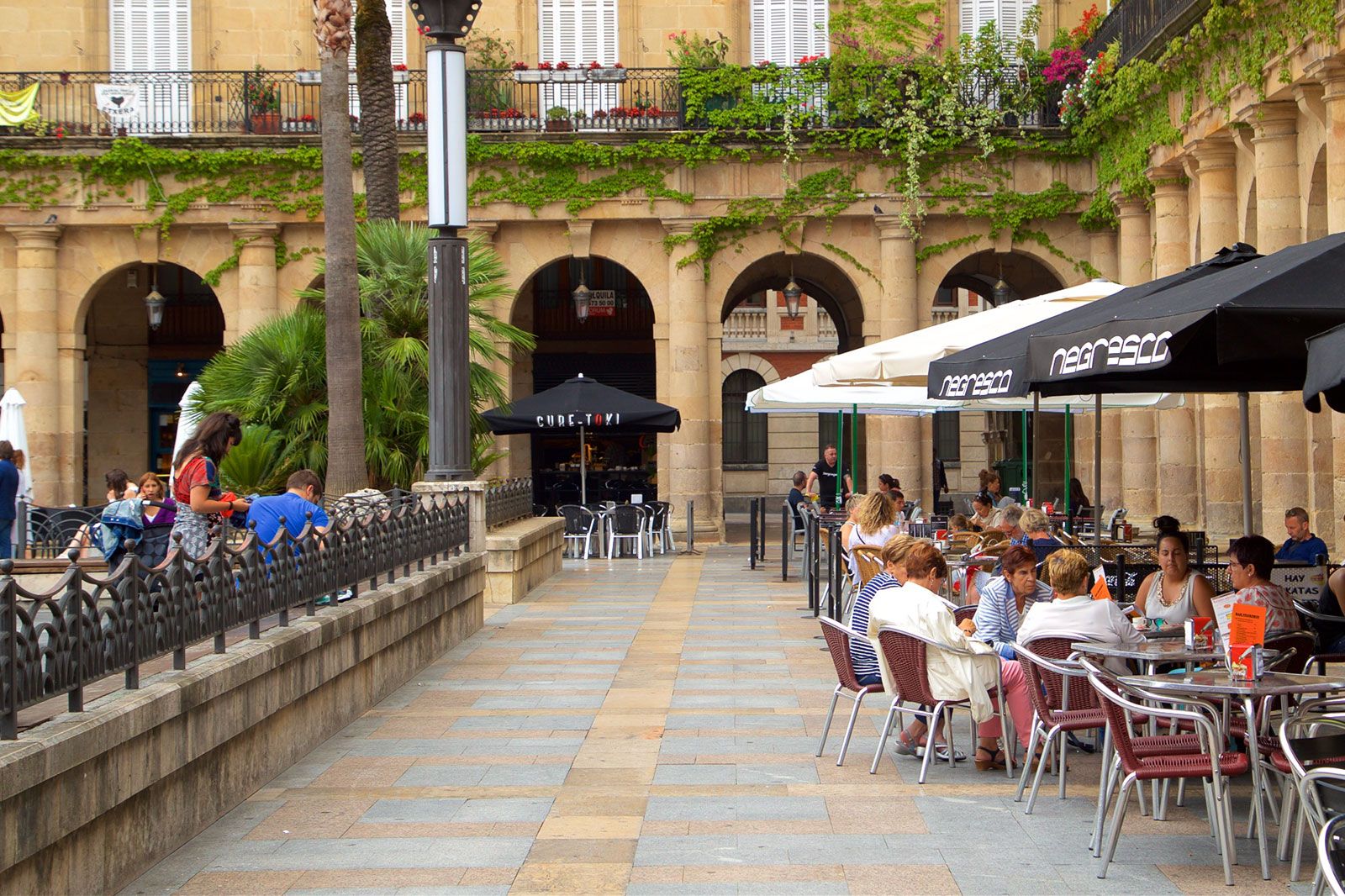 People eat under umbrellas at tables in a town square.