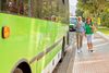 A man and woman on their phones walking past a bus.