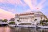 The neoclassical Fullerton Hotel in Singapore with water in the foreground and a pink sunset sky in the background.