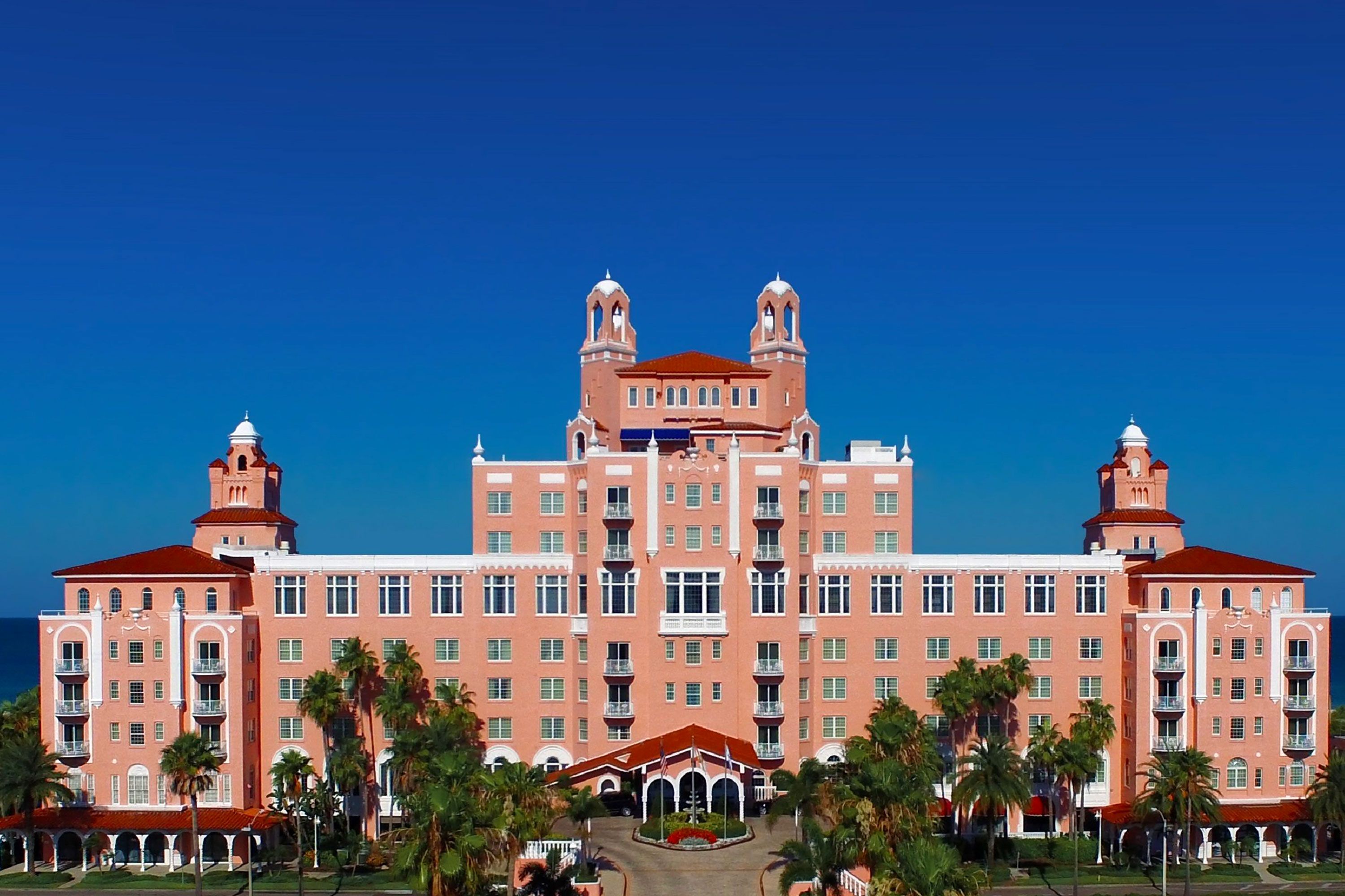 Front exterior view of The Don CeSar hotel in Florida with pink historic architecture and palm trees.