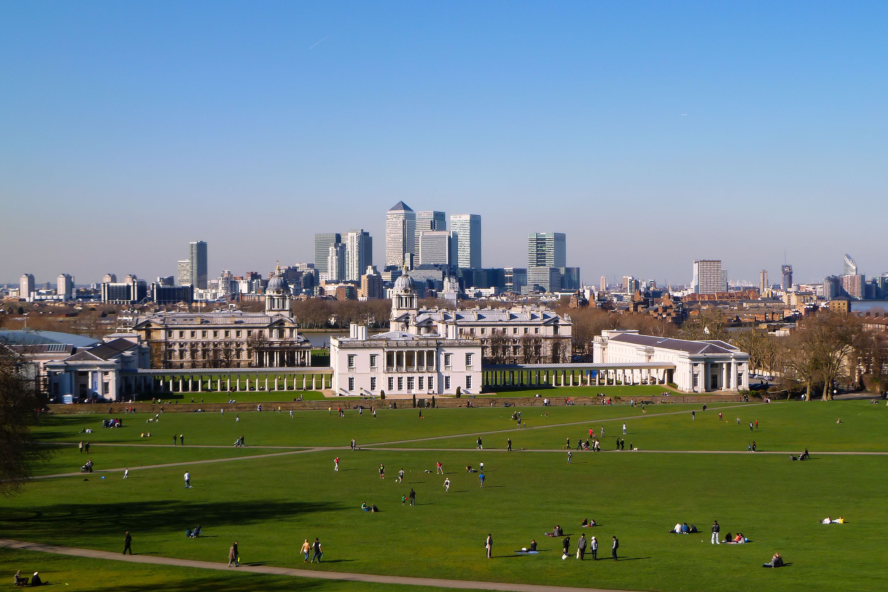 A view of Greenwich Park with the Queen’s House in front and Canary Wharf skyscrapers in the background on a clear day.