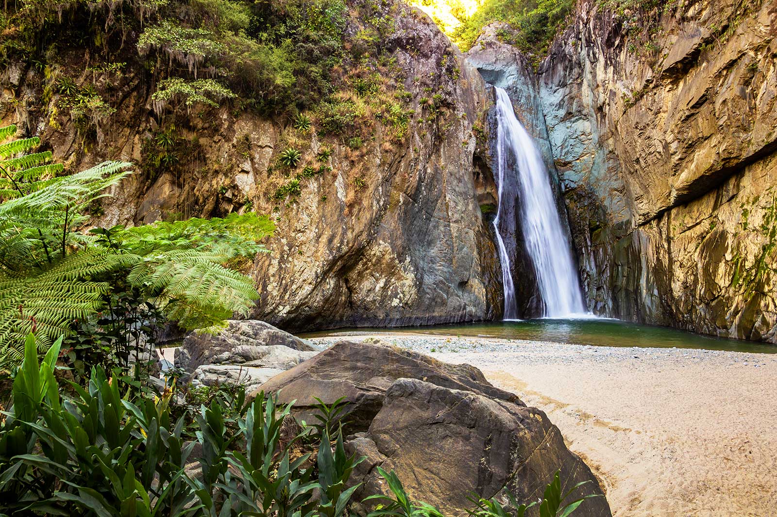 A waterfall with a pool of water and surrounded by rocky cliffs.