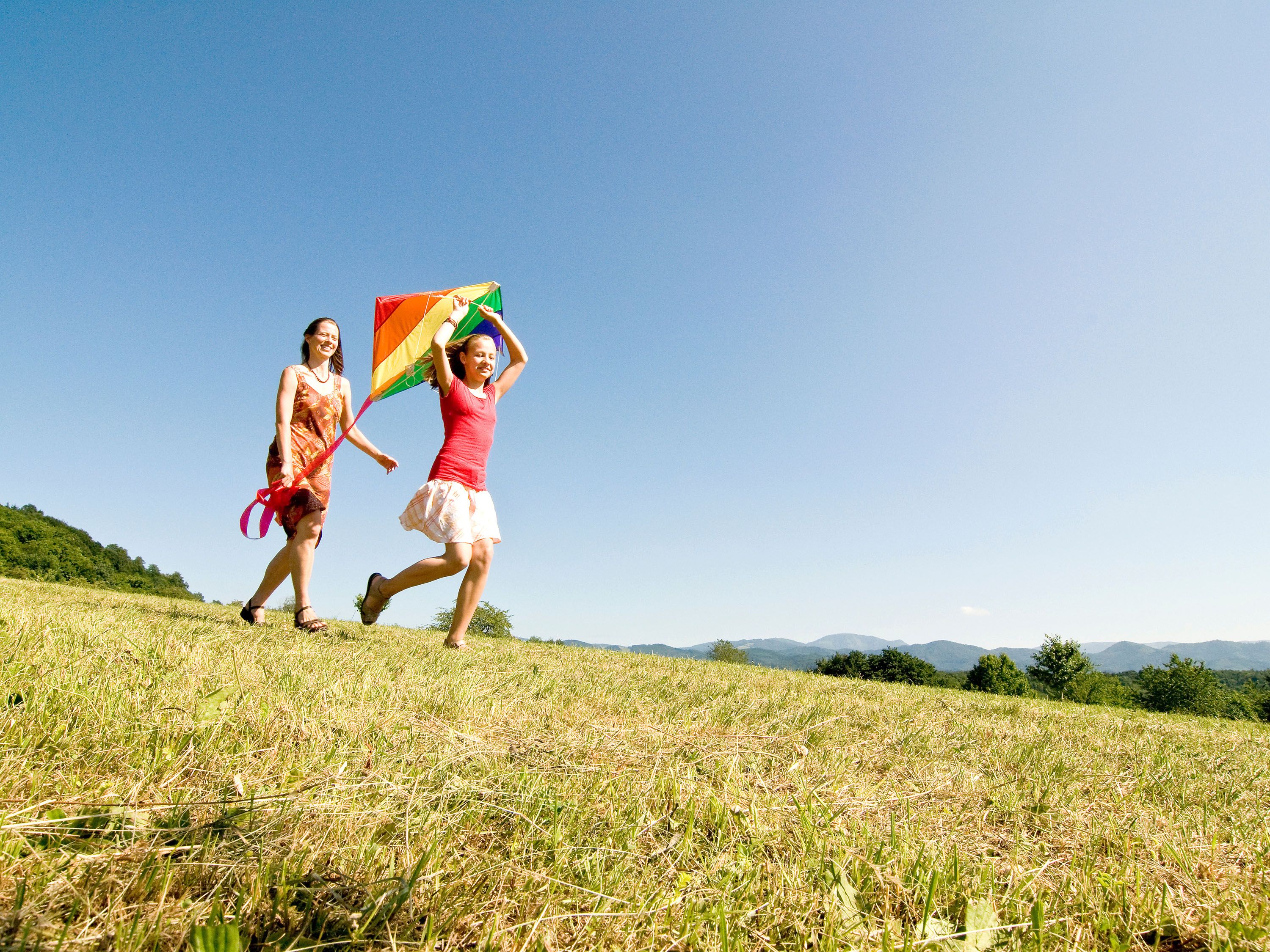 Woman and girl walk on grass with colorful kite.