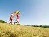 Woman and girl walk on grass with colorful kite.