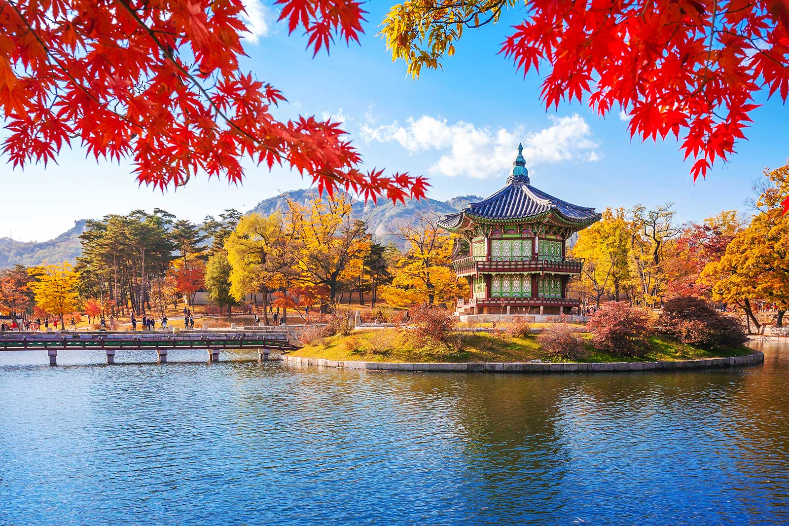 A Korean castle by water surrounded by autumnal trees. 