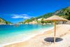 An umbrella in the sand at a beach with blue waters and mountains.