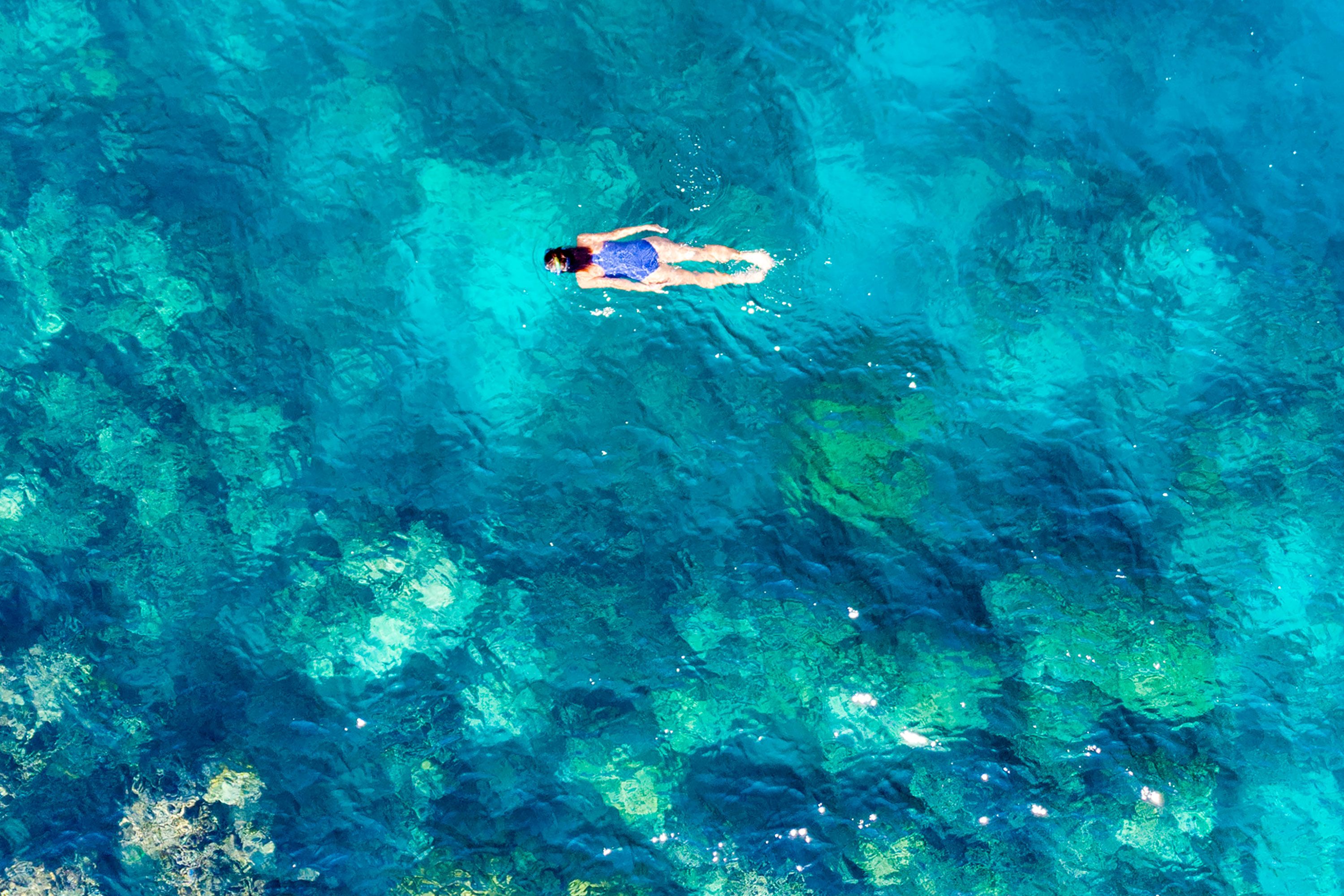 A lone swimmer floats above clear turquoise water near a coral reef.