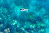 A lone swimmer floats above clear turquoise water near a coral reef.