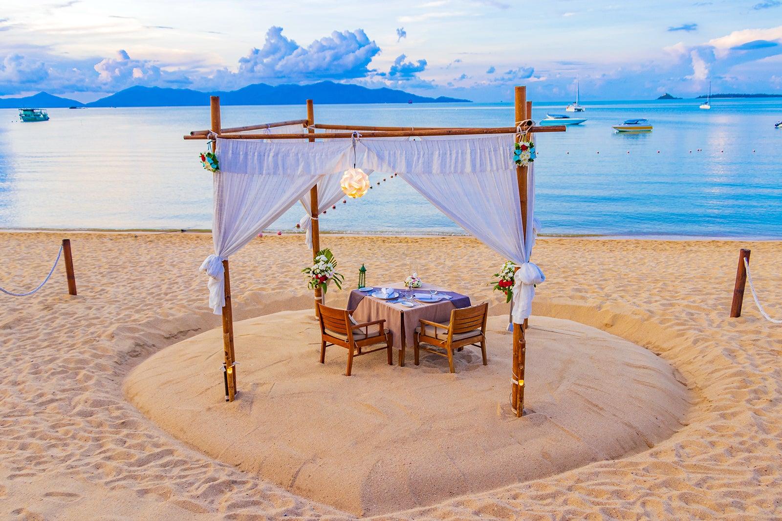 Draped canopy over a dining table on the beach overlooking the ocean.