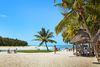 People on a sandy beach with palm trees and small grass-roof huts.