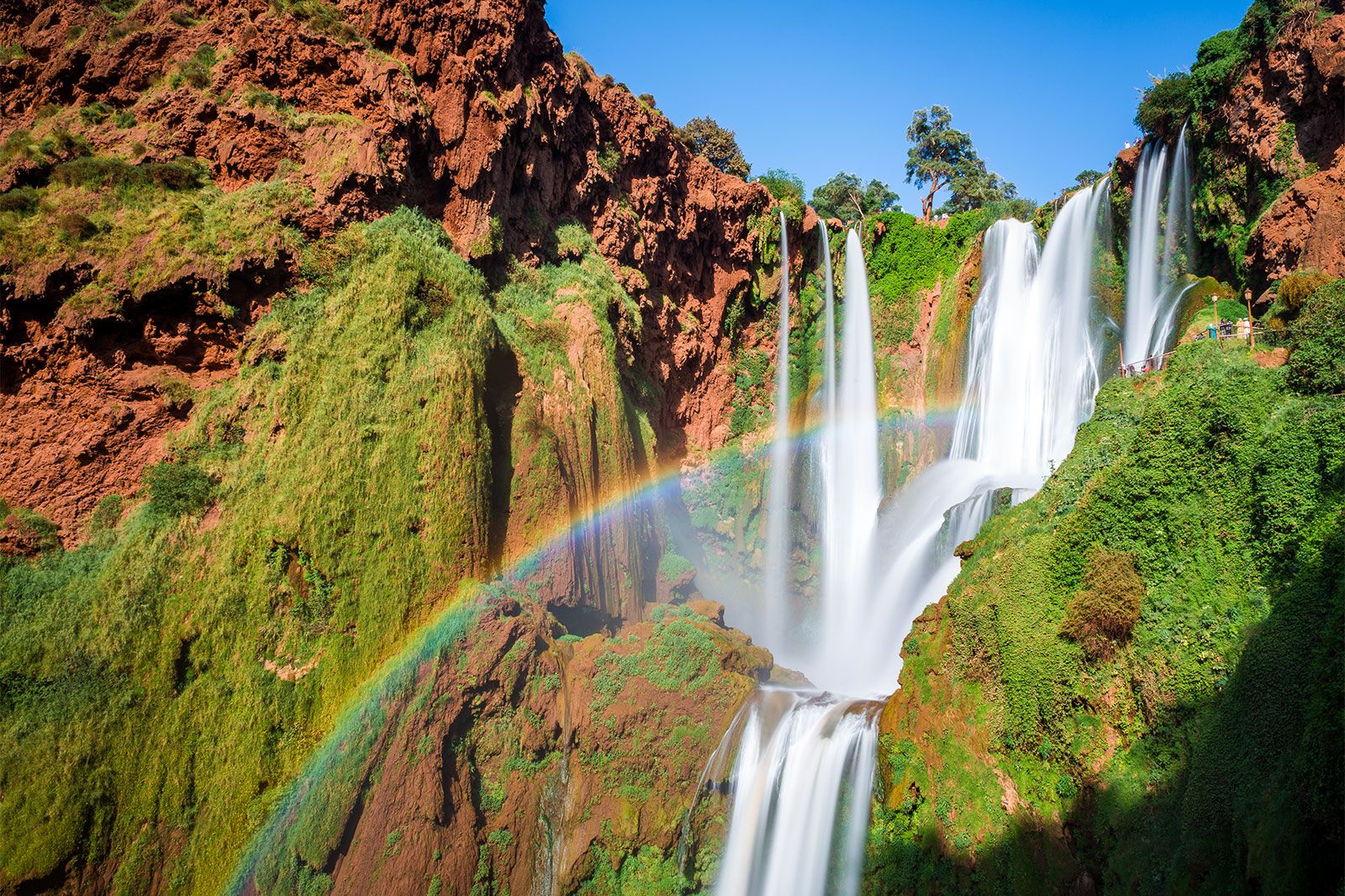 A large waterfall falls down red cliffs with green moss.