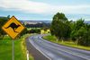 A road disappearing around the bend and a traffic sign with a kangaroo on it.