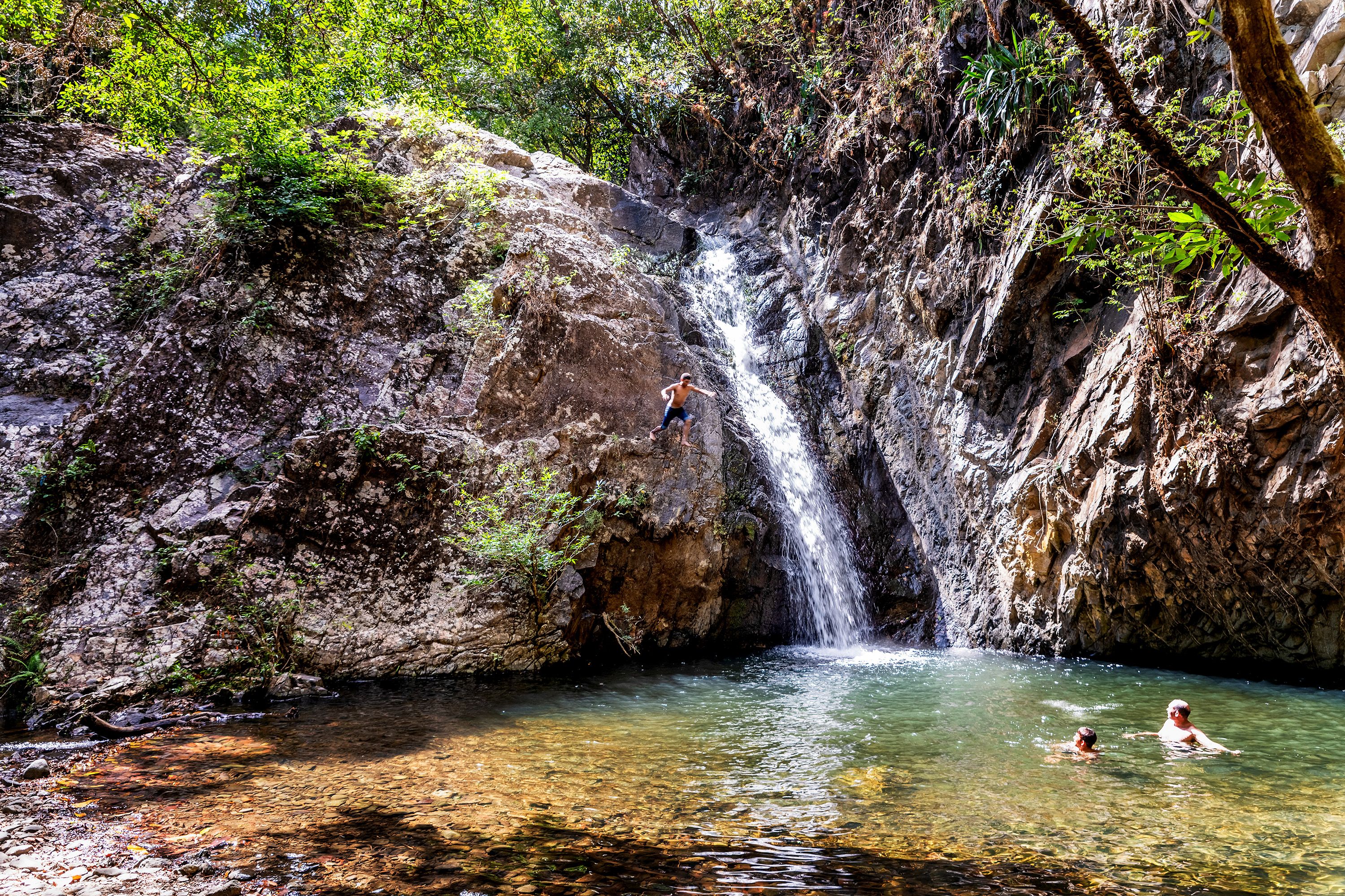 People swim under a waterfall.