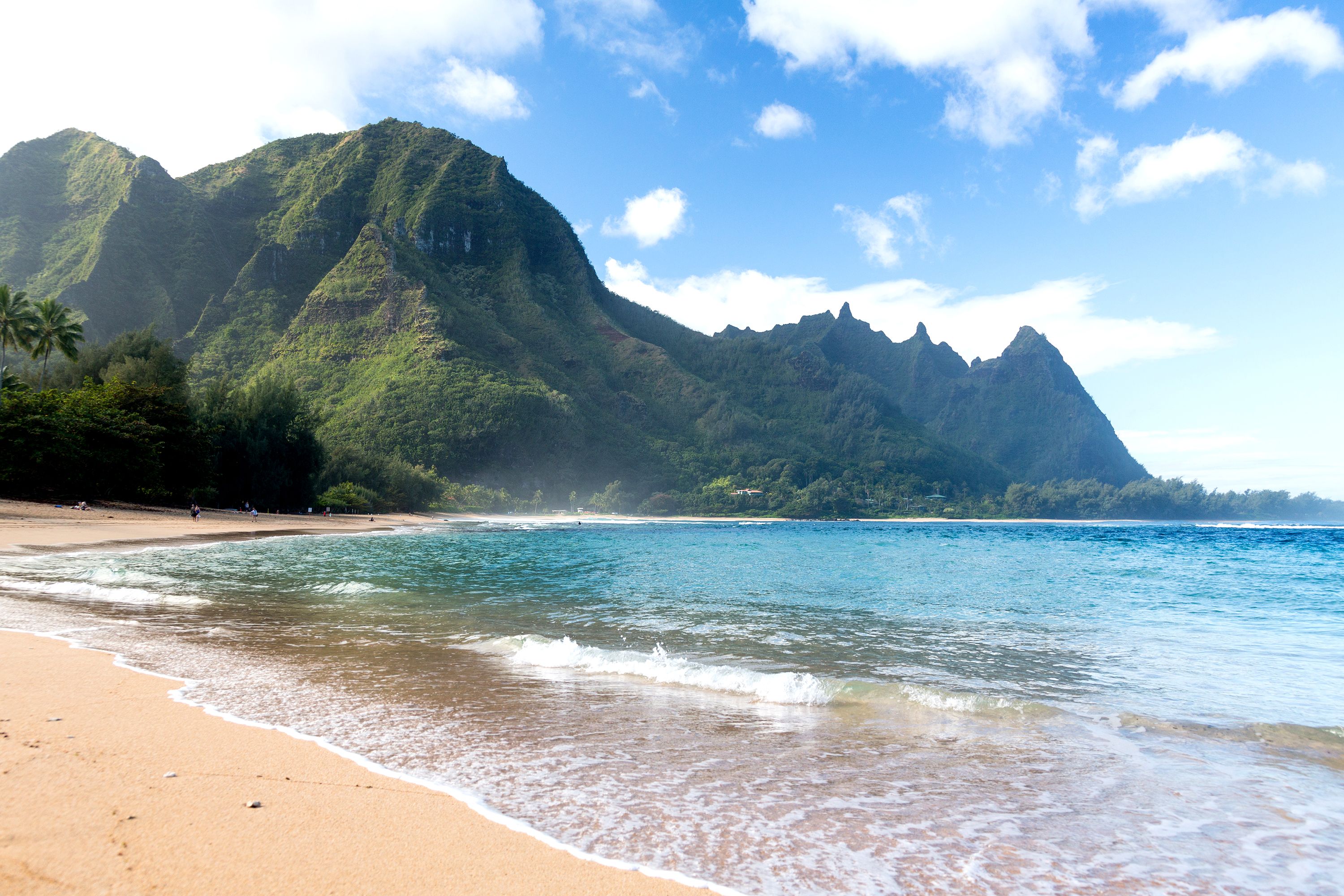 A beach with turquoise waters and mountains in the background.