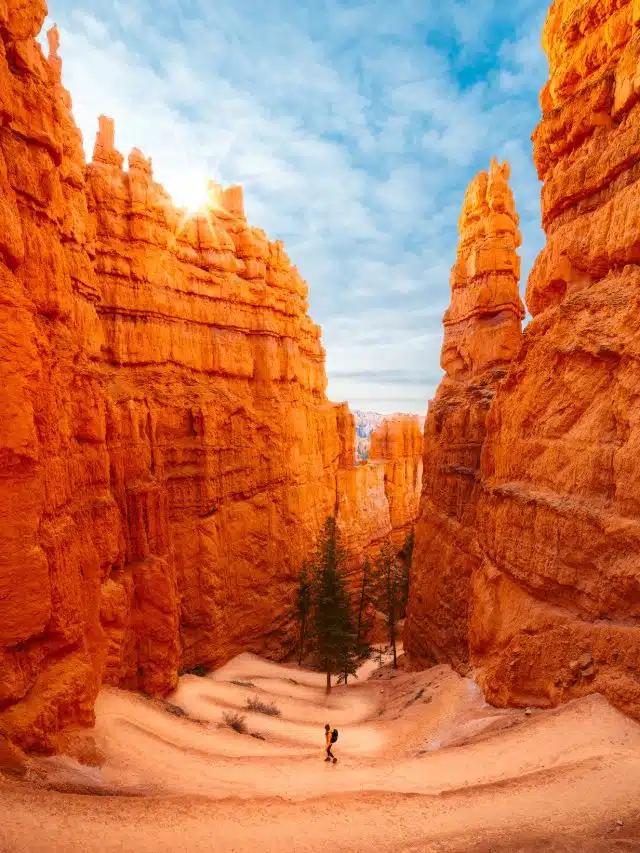 A person walks down a graduated slope between the bright orange canyon walls of Bryce Canyon National Park, Utah 