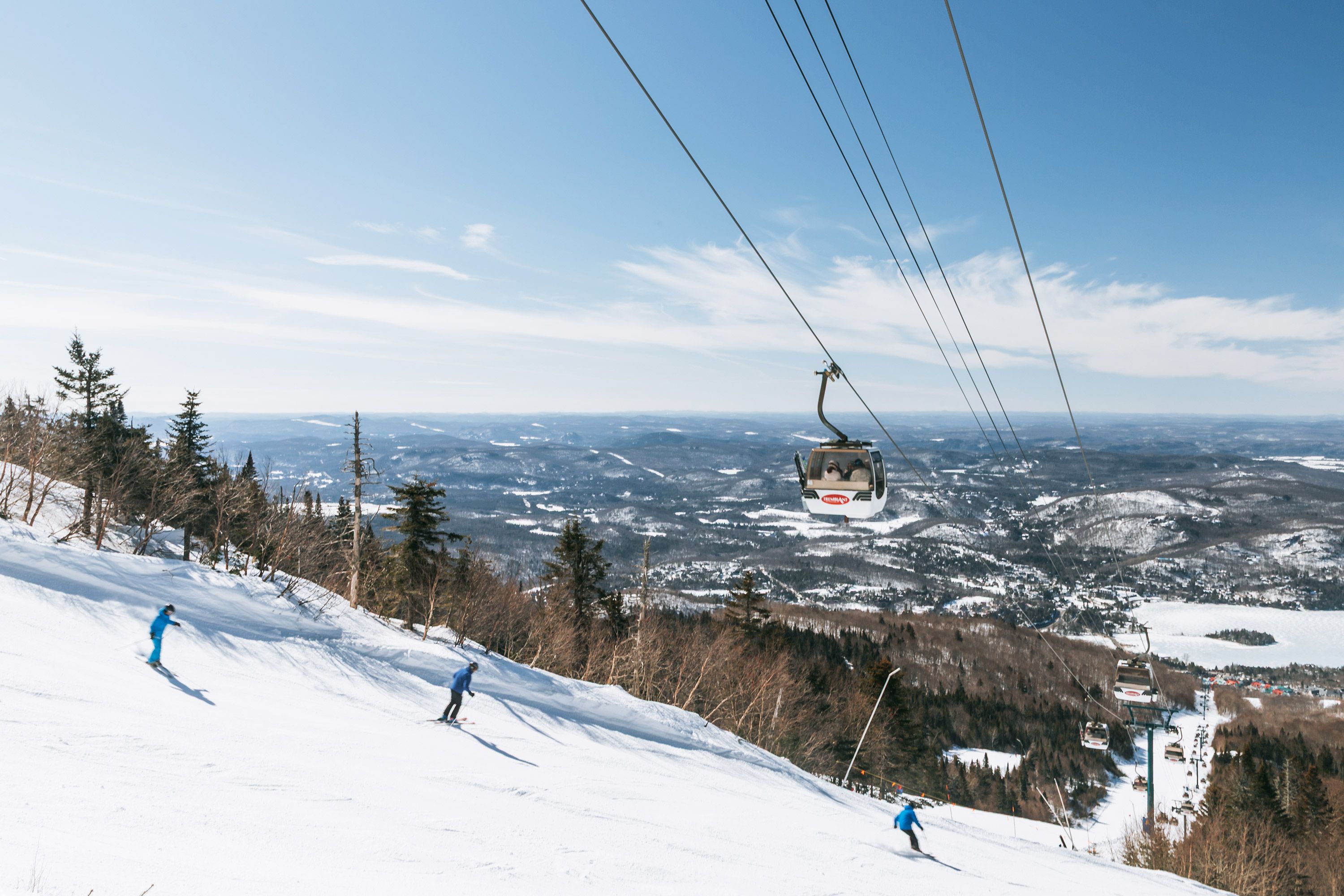 Drei Personen auf Skiern fahren einen verschneiten Hang hinunter, über ihnen befindet sich ein Skilift. 