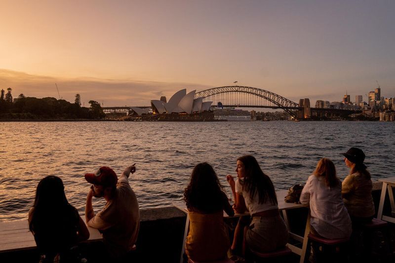 People look out over the water at sunset to the Sydney Opera House and Harbour Bridge in Sydney, New South Wales, Australia