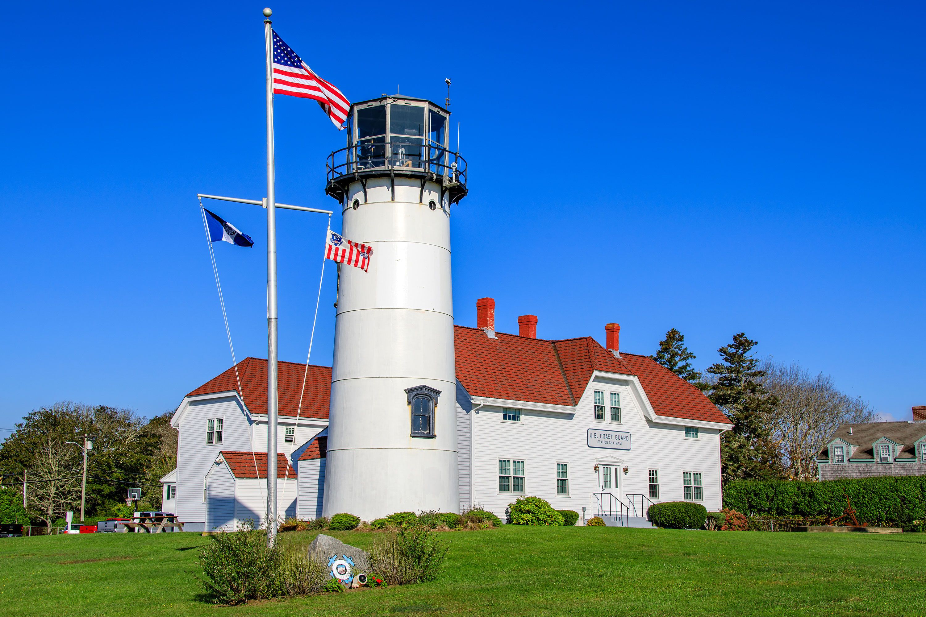 Chatham Lighthouse on Cape Cod’s coastline, with its red-and-white tower rising above rocks and the Atlantic Ocean under a partly cloudy sky.