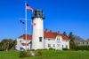 Chatham Lighthouse on Cape Cod’s coastline, with its red-and-white tower rising above rocks and the Atlantic Ocean under a partly cloudy sky.