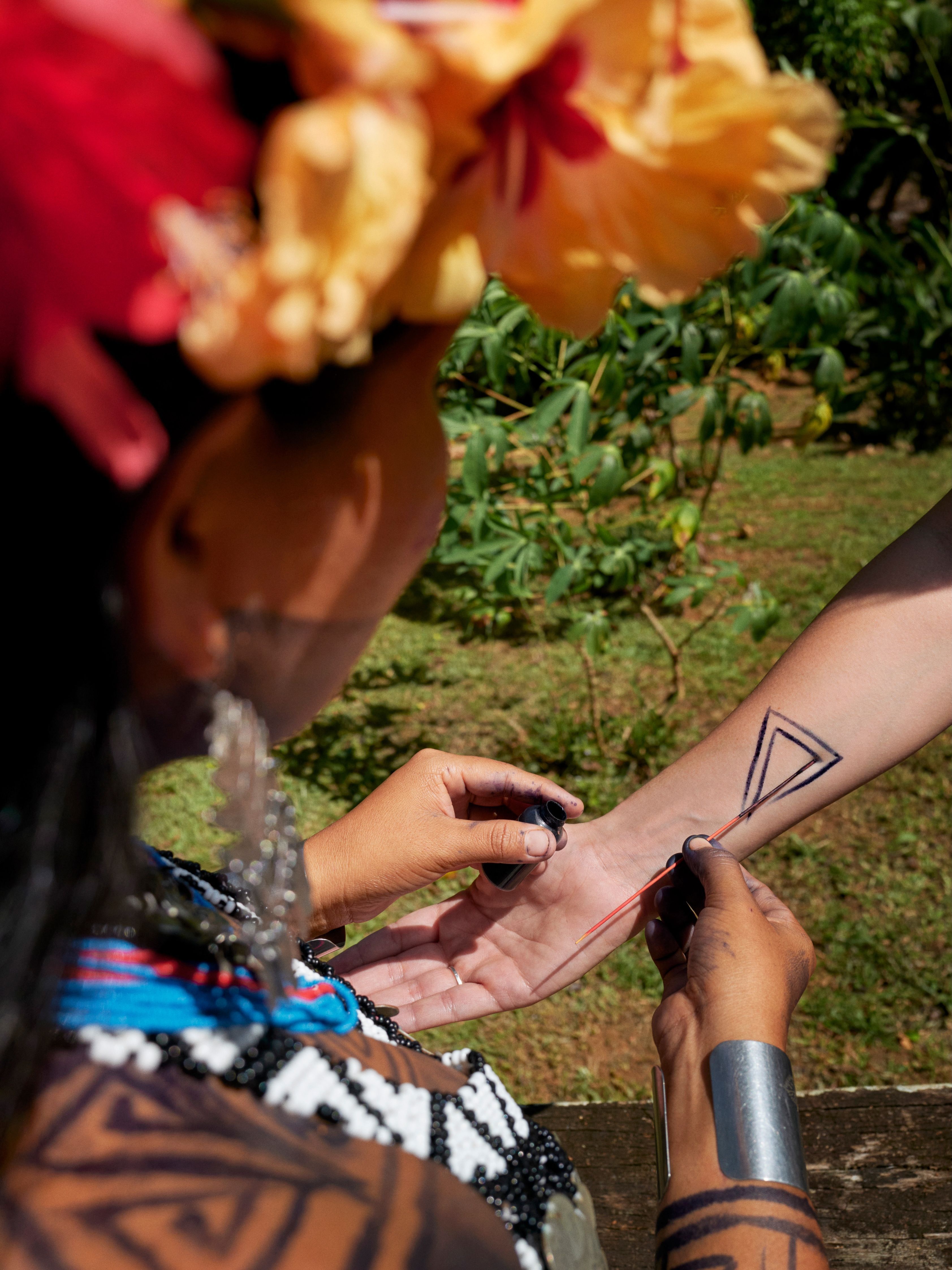 A member of the Emberá tribe, wearing a floral headdress, draws a triangular temporary tattoo on to an outstretched arm