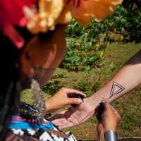 A member of the Emberá tribe, wearing a floral headdress, draws a triangular temporary tattoo on to an outstretched arm