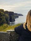 A woman looks out over the sea at the famed Cliffs of Moher, which run for 8.5 craggy miles