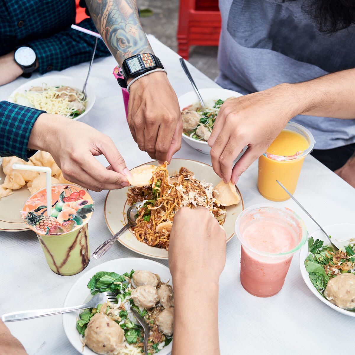 Alfresco diners reach their hands towards a shared bowl of noodles at an alfresco dining spot