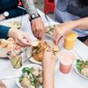 Alfresco diners reach their hands towards a shared bowl of noodles at an alfresco dining spot