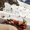 A board of appetizers and a glass of wine is served at an après-ski resort in the French Alps while people ski down the mountain below