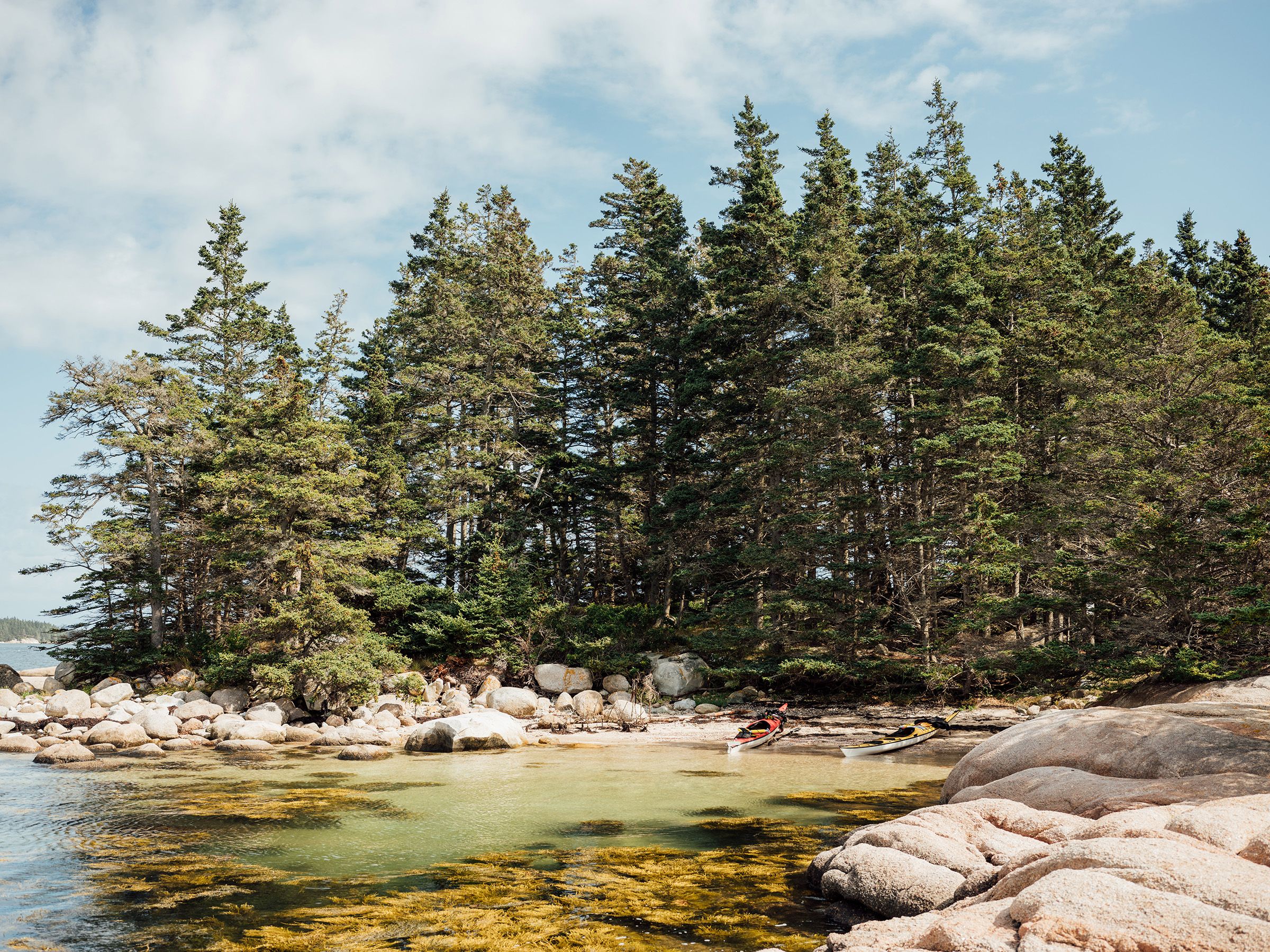 A red and yellow kayak are beached on a remote island in Maine.