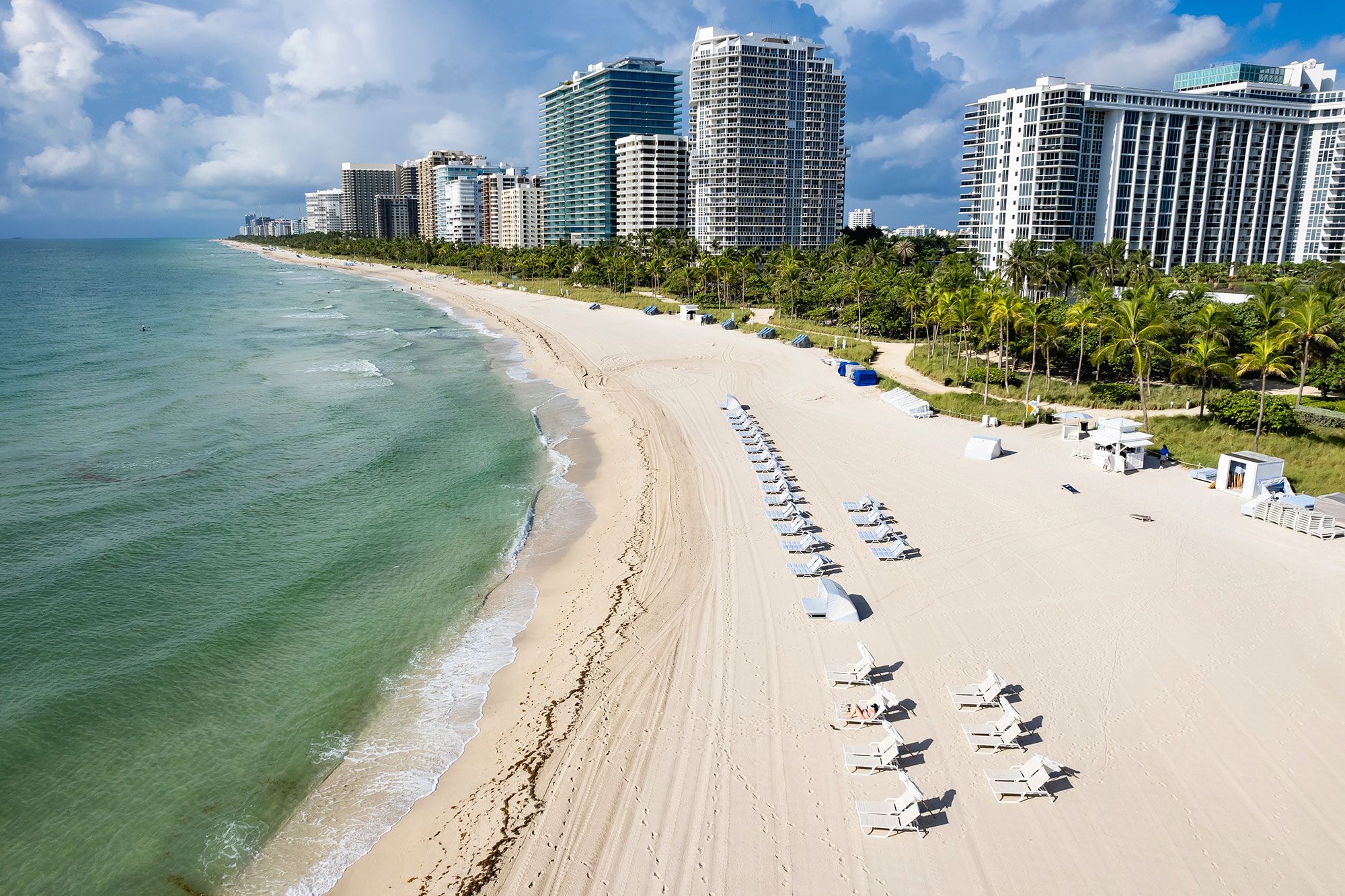 Aerial view of white chairs on the beach with buildings in the background of Bal Harbour Beach, Miami.