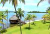 A small circular hut juts into the ocean surrounded by palm trees.