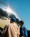 Two men wearing baseball caps look at the reflections in The Bean, a silver bean-shaped sculpture officially known as Cloud Gate, in Chicago
