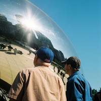Two men wearing baseball caps look at the reflections in The Bean, a silver bean-shaped sculpture officially known as Cloud Gate, in Chicago