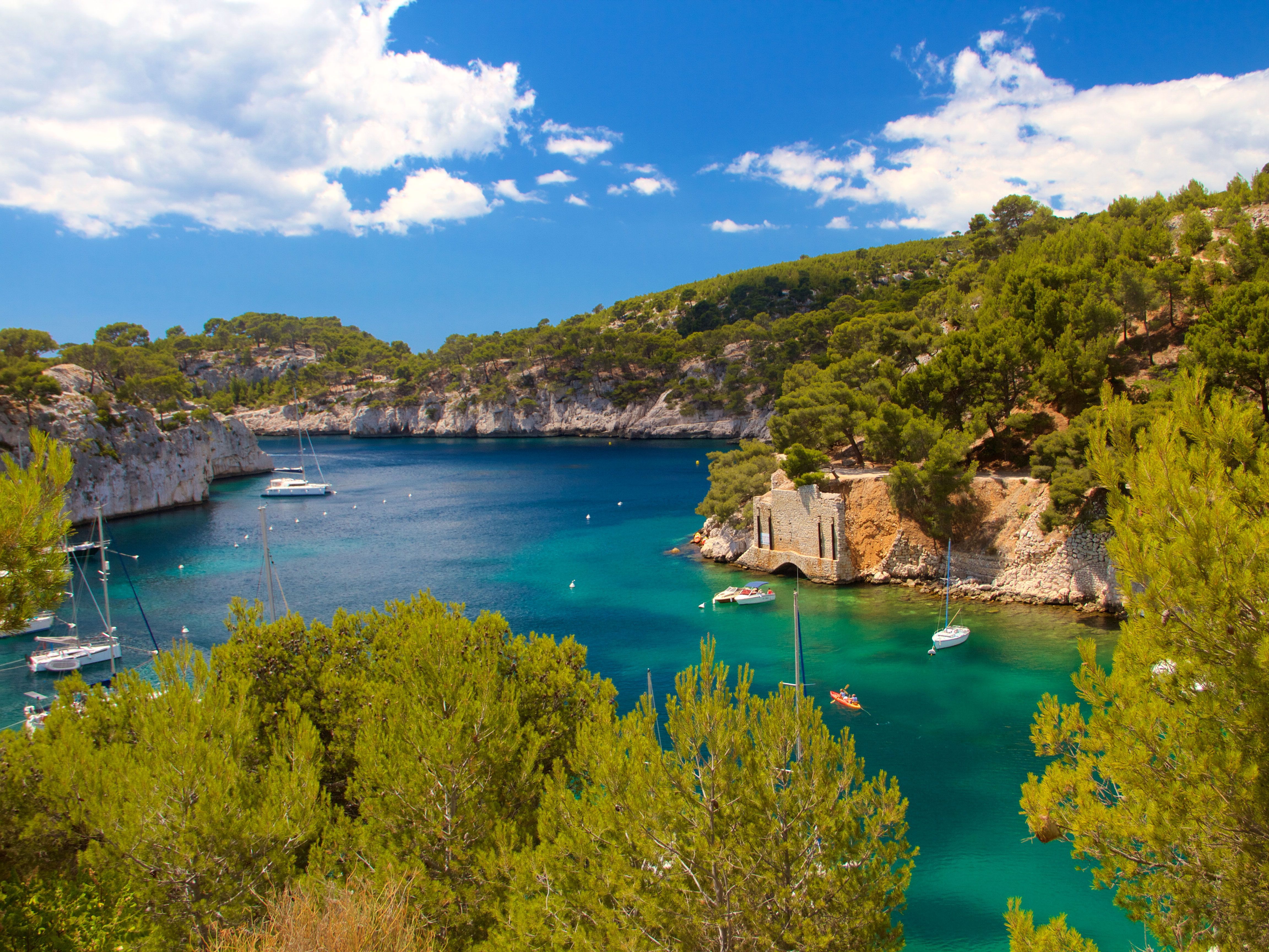 A bright blue stretch of water is bordered by green trees atop brown cliffs bordering the water