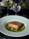 A fillet of salmon is served on a bed of green vegetables and sauce