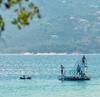 Four people stand on a diving platform in the distance on bright blue water of the Albanian Riviera