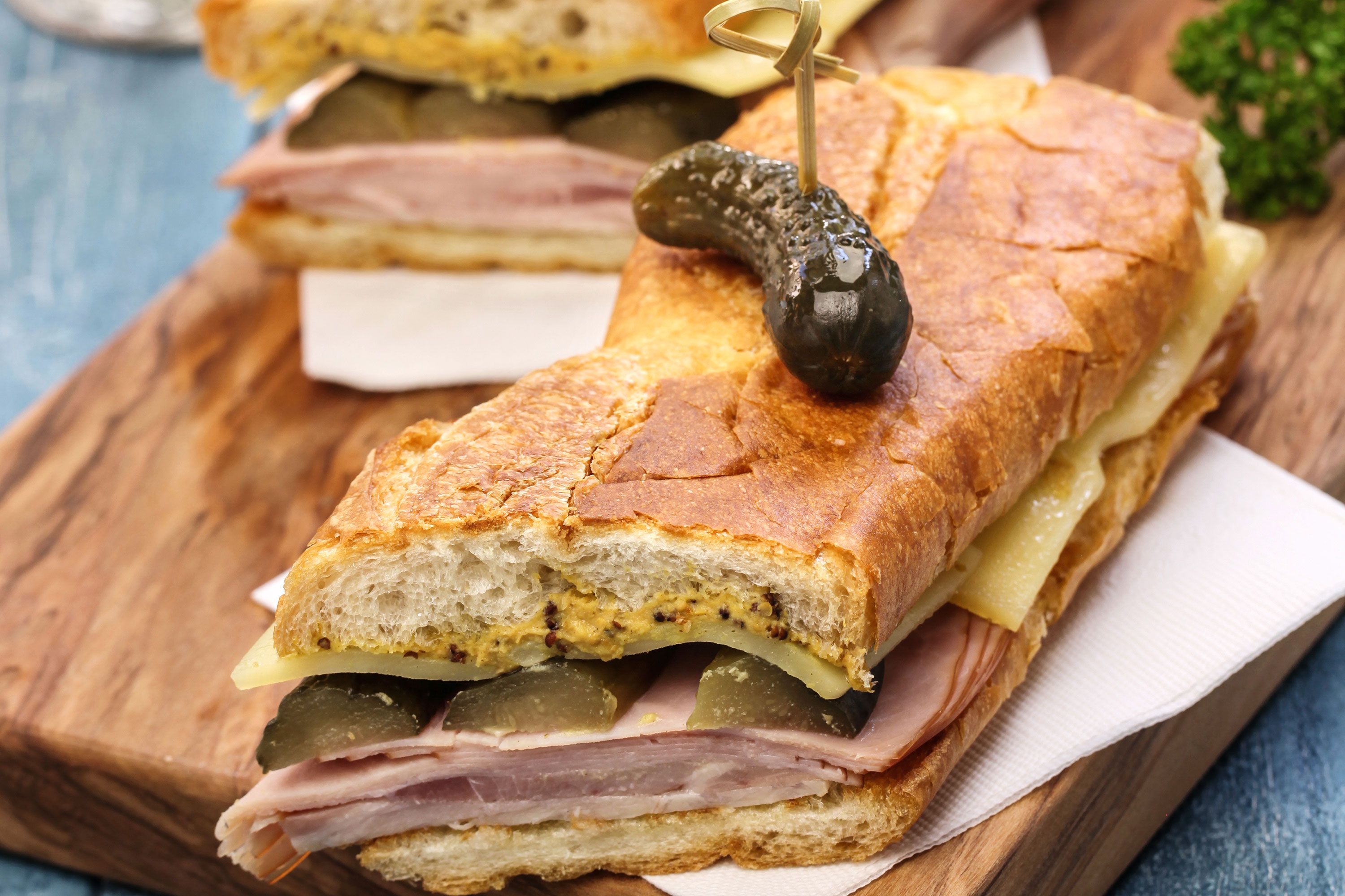 A cuban sandwich with pickles ham and cheese on wood cutting board.