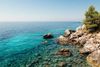 A person in a red and yellow kayak paddles through clear waters along the rocky coastline in Croatia