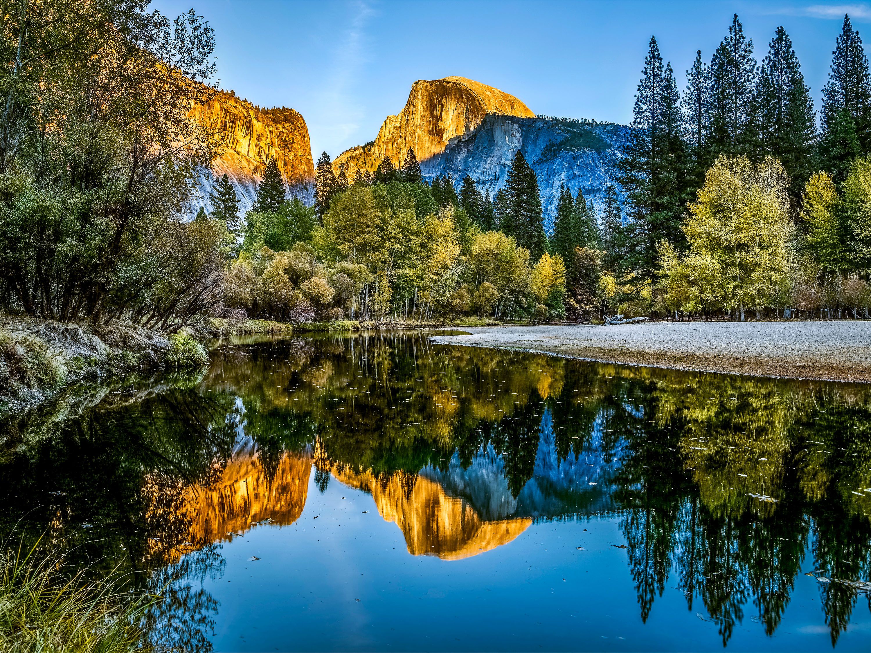 Sun shines on a peak reflected in a calm lake surrounded by trees.