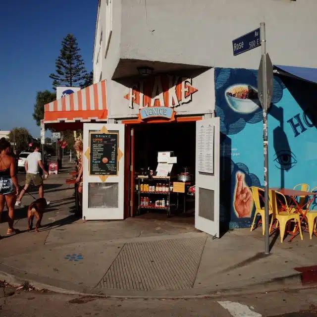 A dog walker passes by the open doors of Flake, with its striped red and white awning