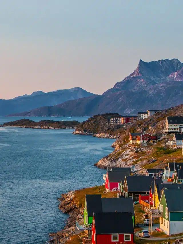 Red, green and yellow wooden houses face out to the sea on a rocky shoreline in Greenland