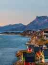 Red, green and yellow wooden houses face out to the sea on a rocky shoreline in Greenland