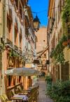 Chairs and tables sit outside a restaurant and plants hang from neighboring windows on the narrow Rue du Chaudron in Strasbourg, France